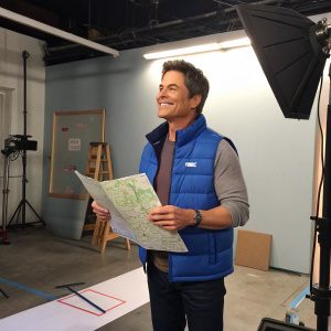 Rob Lowe as Chris Traeger, from the show Parks and Recreation. Wearing blue vest, holding map. Studio set, behind-the-scenes shot