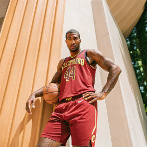 Professional basketball player Iman Shumpert, muscular and tattooed, posing in his Cavaliers jersey, number 4, against a sleek black backdrop.