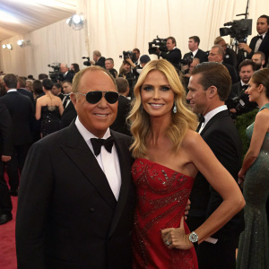Michael Kors and Heidi Klum, both in formal attire, at the Met Gala. Crowded room with flashing cameras.