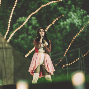 Nicki Minaj, in a vibrant ensemble of pastel and bold hues, performs on stage. The backdrop is a dynamic light show.