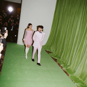 Gigi Hadid and Zayn Malik attending a bustling gala. Surrounded by flashing cameras and paparazzi. Luxurious red carpet setting