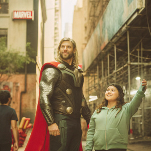 Chris Hemsworth as Thor and a young woman in a bustling urban area. Gothic architecture with dark, shadowy alleyways. A Marvel promotional banner visible