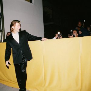 Denis Leary, grinning broadly, in a sleek black suit. At a bustling awards show. Surrounded by flashing cameras and cheering fans.
