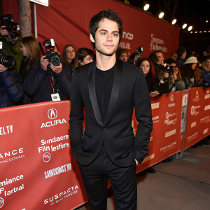 Dylan O'Brien, actor, dressed in a black suit at the Sundance Film Festival. Crowded backdrop with flashing cameras