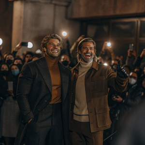 Kellan Lutz and Brad Pitt standing at a crowded movie premiere. Kellan, youthful with a medium build, Brad, older and bald. They pose with big smiles amidst a sea of fans and paparazzi.