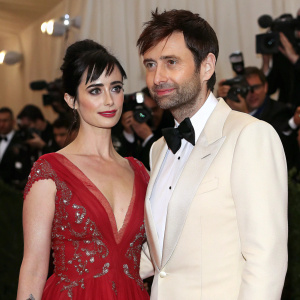 Krysten Ritter and David Tennant at the Met Gala. Both are wearing designer gowns. Flashing lights and crowd visible in the background.