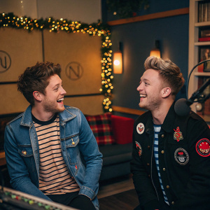 Niall Horan and Roman Kemp at a cozy radio station studio. They are laughing and chatting. Niall in denim jacket and striped shirt. Roman in black jacket with patches. Festive decorations around