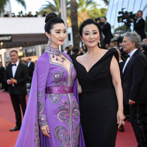 Fan Bingbing and Gong Li at Cannes Film Festival. Both in stunning outfits. Fan in purple outfit with intricate designs, Gong in black dress. Grand outdoor event with celebrities around.