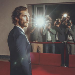 Matthew McConaughey, actor, at a movie premiere. Wearing a navy blue suit. Vibrant red carpet with flashing cameras