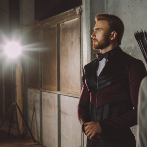 Chris Evans as Hawkeye, MCU outfit, black and maroon suit, standing in a dimly lit warehouse. Camera flash in background