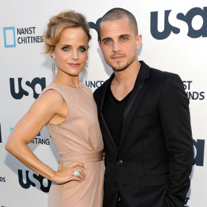 Mena Suvari and Simone Sestito, dressed in formal attire, posing at the USA Network award show. Mena in taupe-colored, sleeveless dress. Simone in a black blazer. White backdrop with USA Network branding.