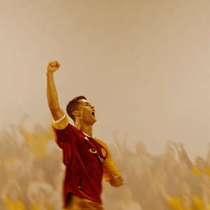 Cristiano Ronaldo, celebrating a goal in a blur of motion. Wearing Manchester United's red jersey with golden logos. The excited crowd is a blurry backdrop.