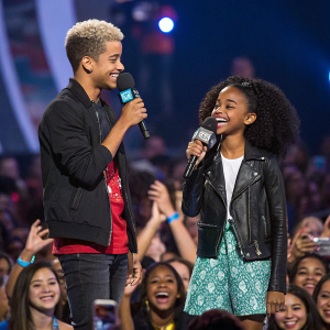 Jordan Fisher and Skai Jackson at WE Day conference, sharing the stage with enthusiastic crowd in the background.