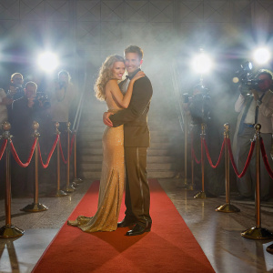 Annalynne McCord and Kellan Lutz at the gala event. They are hugging on the red carpet. Bright lights and camera flashes in the background.