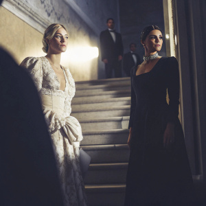 Lili Reinhart and Camila Mendes at the Met Gala. Lili with platinum blonde hair and intricate white dress. Camila with sleek, long black dress. Grand staircase backdrop