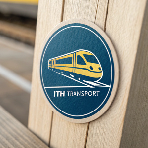 Ith Transport's logo featuring a sleek, blue and yellow train icon. Company name, 'Ith Transport,' written beneath in modern font. Logo set against a grainy, wooden background.