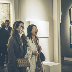 Jennifer Blei Stockman and Amanda Kim, grinning, at an art gallery opening with MOMA-inspired backdrop.