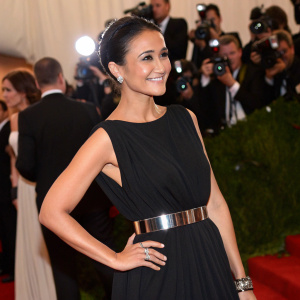 Emmanuelle Chriqui at a gala event. Wearing a simple black dress with a metallic belt. Amidst a crowd of guests and flashing cameras.