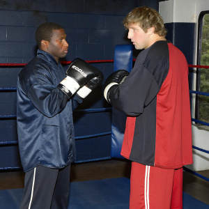 Floyd Mayweather and Logan Paul in a boxing ring. Intense stare, gloves on.