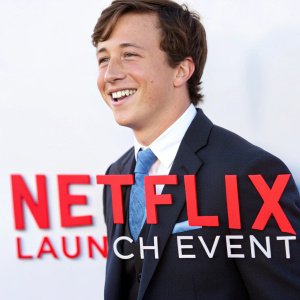 Skyler Gisondo, smiling in a dark suit with blue tie, at a Netflix launch event. White background with red text