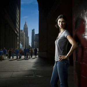 Morena Baccarin on the set of a high-profile TV show. Wearing a casual outfit, jeans and a t-shirt. Background is a bustling cityscape.