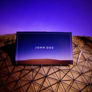 John Doe's business card features a sleek, modern design with a gradient dark blue background and intricate wireframe patterns. The text is clean and legible.