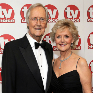 Nicholas Parsons and Ann Reynolds at the awards night. Smartly dressed in black tuxedo and black gown. Posed elegantly in front of TV Choice logo backdrop.