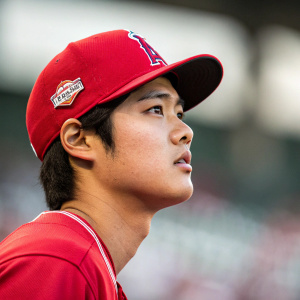 High-resolution image of Shohei Ohtani, young Asian baseball player, in intense focus. Wearing a red cap and jersey. Blurred stadium background.