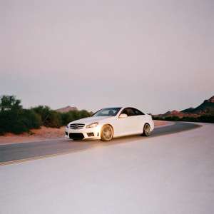 Custom tuned Mercedes-Benz C63 W204 coupe on a scenic highway. Background features rolling hills and distant mountains. Golden hour lighting.