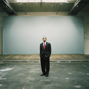 Barack Obama, ex-president, intense expression, dark suit, red tie, white shirt. Empty stage, blue backdrop