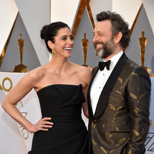 Sarah Silverman and Michael Sheen at the Oscars. Sarah in a black satin off-shoulder gown, Michael in a classic tuxedo with gold accents. Warm, smiling pose