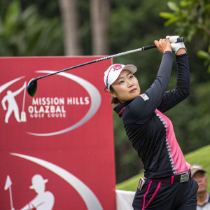 Ji Hyun Oh, focused during her golf swing. Mission Hills Olazabal Golf Course. Wearing a black and pink golf outfit. Red banner with logo and text in background.
