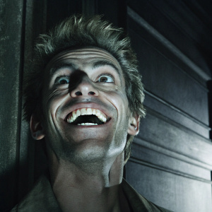 Close-up of Junkrat's face. Large grin, showing sharp teeth. Spiky hair. Dark backdrop