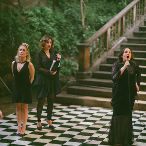 At the Sanremo Music Festival, Luciana Littizzetto, Tania Cagnotto, Francesca Dallape, and Frankie Hi-NRG mc are on stage. Black and white checkered floor. They are dressed in elegant black dresses. Different poses and expressions.