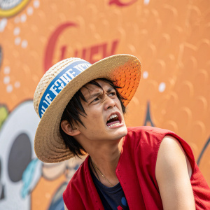 Luffy from One Piece, frustrated face, wearing a hat with Spanish text. Vibrant, textured, abstract background with playful, animated aesthetic.