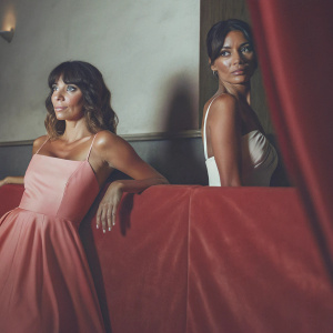 Eva Longoria and Keli Lee posing at an awards show. Pastel pink dress and neutral toned backdrop.