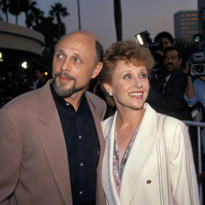 Hector Elizondo and Carolee Campbell captured in a candid moment outside the 'Beverly Hills Cop III' premiere. The duo stands amidst flashing cameras and fans, their expressions lively and animated against a bustling backdrop.