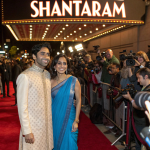 Shubham Saraf and Rachel Kamath attending the premiere of 'Shantaram' on Apple TV+. Shubham in ethnic wear, Rachel in a blue saree. Crowded red carpet event with flashing cameras.