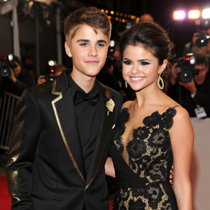 Justin Bieber and Selena Gomez attend award show. Justin wears black suit with gold accents. Selena in black lace dress. Red carpet event