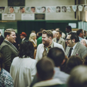 James Corden, Ronnie Corbett, and Andrew Flintoff at a lively backstage gathering. Crowded room with various attendees.