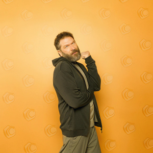 Jon Bernthal, with scruffy beard and wearing a black hoodie, poses at the Comic-Con event. The backdrop features vibrant comic book characters and logos.