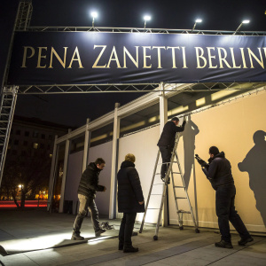 Artists working on a massive 'PENA ZANETTI BERLIN' banner at night. Dark attire, intense focus. Spotlights illuminate the banner and workers. Contemporary art gallery opening event.
