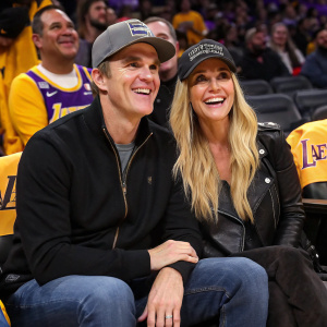Luc Robitaille and Stacey Toten, dressed in casual attire, at a Lakers game. They're smiling broadly and cheering.