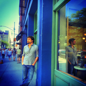Pedro Pascal, in a casual shirt and jeans, outside a bustling coffee shop in New York City.