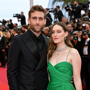 Oliver Jackson-Cohen and Victoria Pedretti at a glamorous gala. Oliver in a sharp suit, Victoria in a vibrant green dress. Crowded red carpet event.