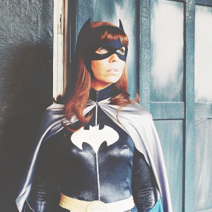 Yvonne Craig in her iconic Batgirl costume from the classic TV show 'Batman'. Dark blue backdrop. Serious expression.