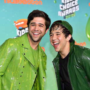 Josh Peck and David Dobrik, covered in green slime, smiling at the Nickelodeon Kids' Choice Awards. Teal backdrop with bright branding