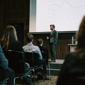 Andre Villas-Boas, dressed in a sharp suit, addresses a packed conference room. Projector screen behind him displays intricate data charts. Conference theme: Sports Analytics Summit