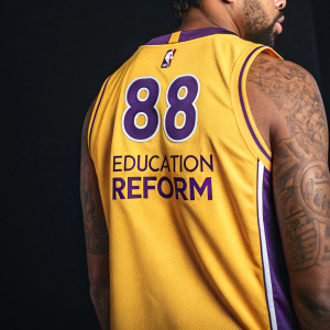 Close-up photo of Markieff Morris's Lakers jersey. Number 88 and 'EDUCATION REFORM' prominently displayed. Jersey is yellow with purple accents, NBA logo visible. Dark backdrop