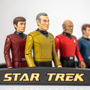 A collection of Star Trek action figures displayed against a white background. The characters, intricately designed, are dressed in their signature uniforms. The scene captures the essence of a starship bridge with the Star Trek logo in the foreground.